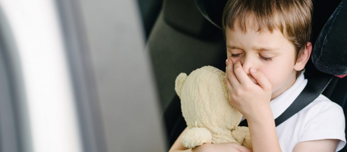 Seven years old small child in the backseat of a car sitting in children safety car seat covers his mouth with his hand - suffers from motion sickness